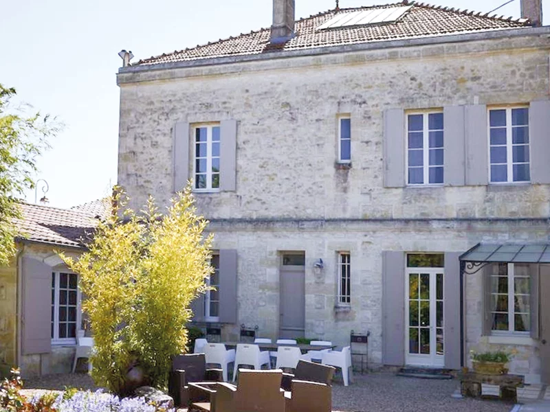 Maison en pierre avec volets, fenêtres et terrasse avec tables, chaises et bambous.