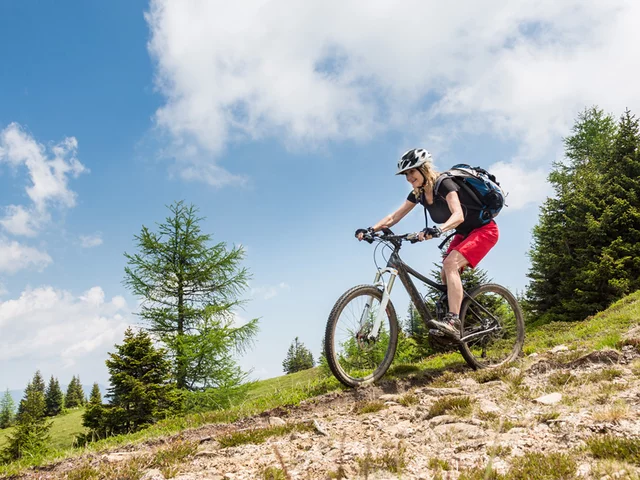 Frau auf einem Mountainbike fährt bergab auf einem Feldweg.