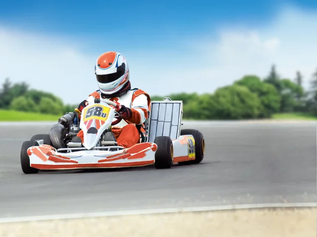 Ein Go-Kart-Rennfahrer in rotem und weißem Anzug auf einer Rennstrecke, der ein Go-Kart fährt.