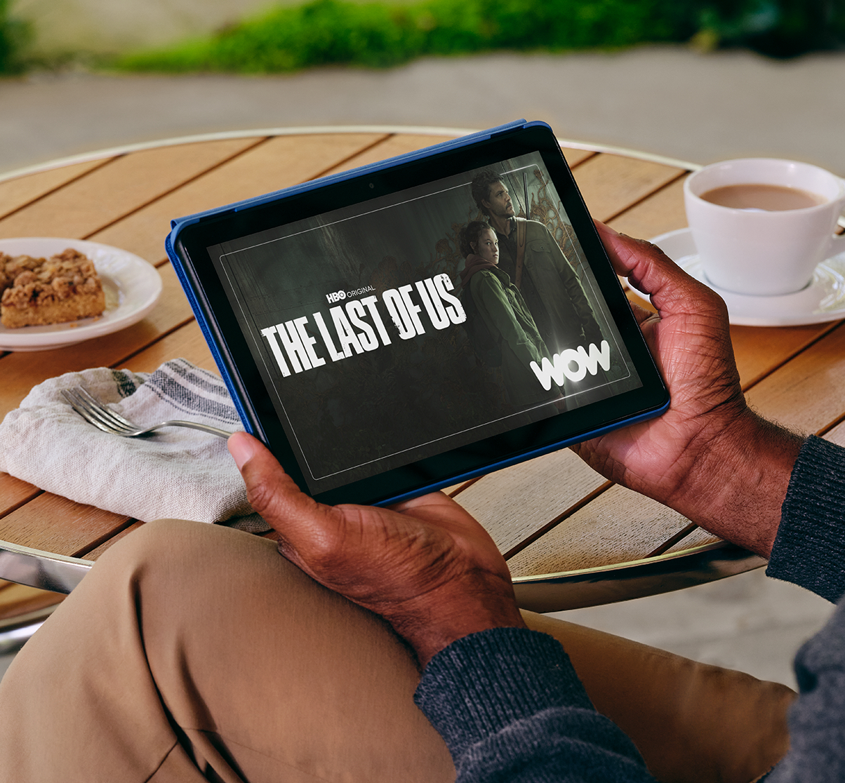 Eine Person hält ein blaues Tablet, auf dem ein Serientitel und ein Bild auf dem Bildschirm angezeigt werden.