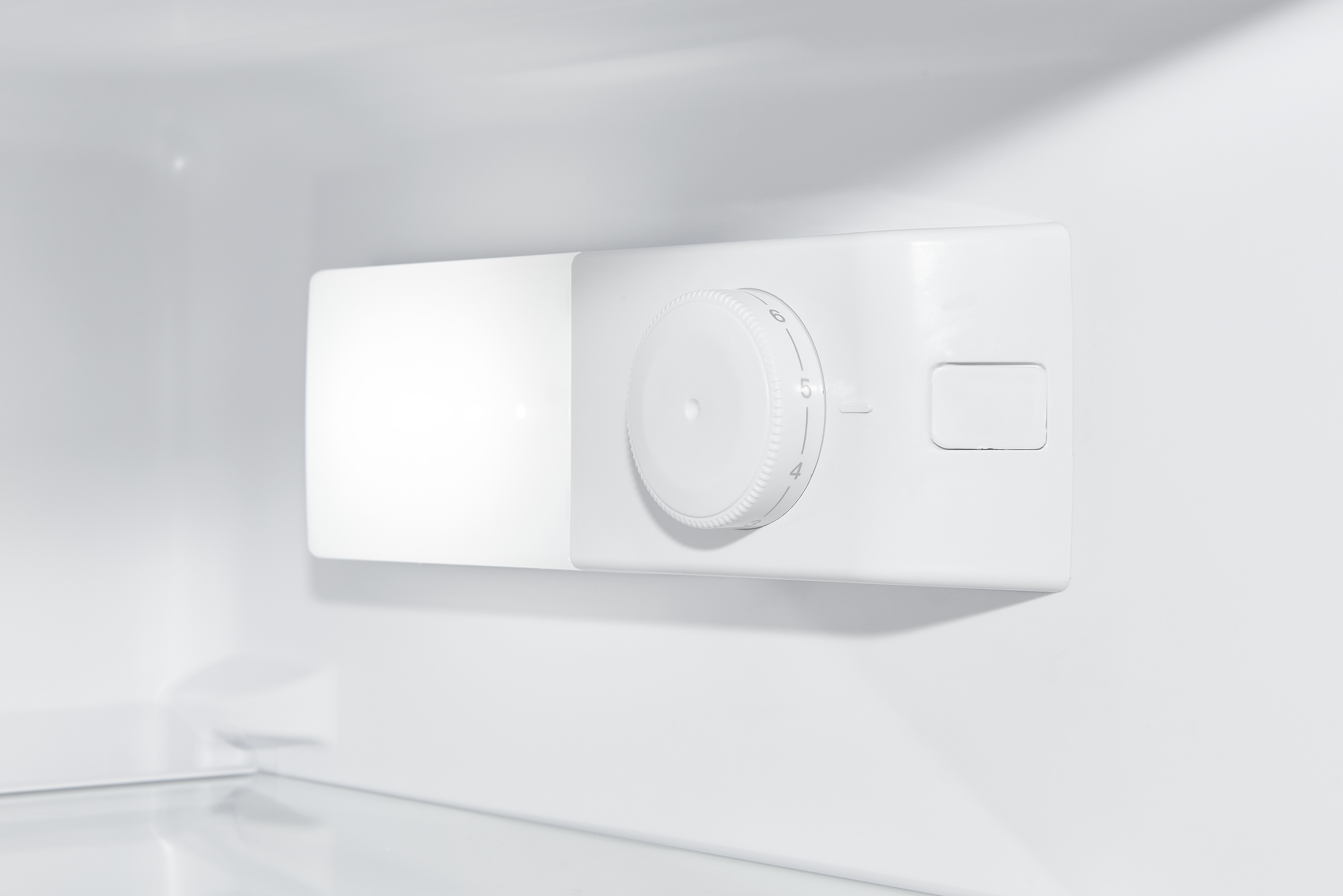 Weißer Innenraum eines Kühlschranks mit Temperaturregler an der Wand.