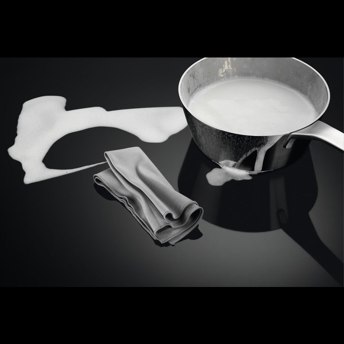 Melk morst uit een pan op een zwart oppervlak. Een grijze doek ligt in de buurt. Wit schuim is zichtbaar.