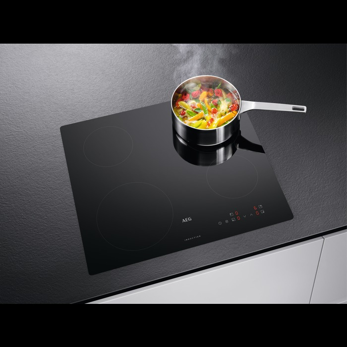 Een zwarte inductiekookplaat met een pan met eten erop, op een donker oppervlak.