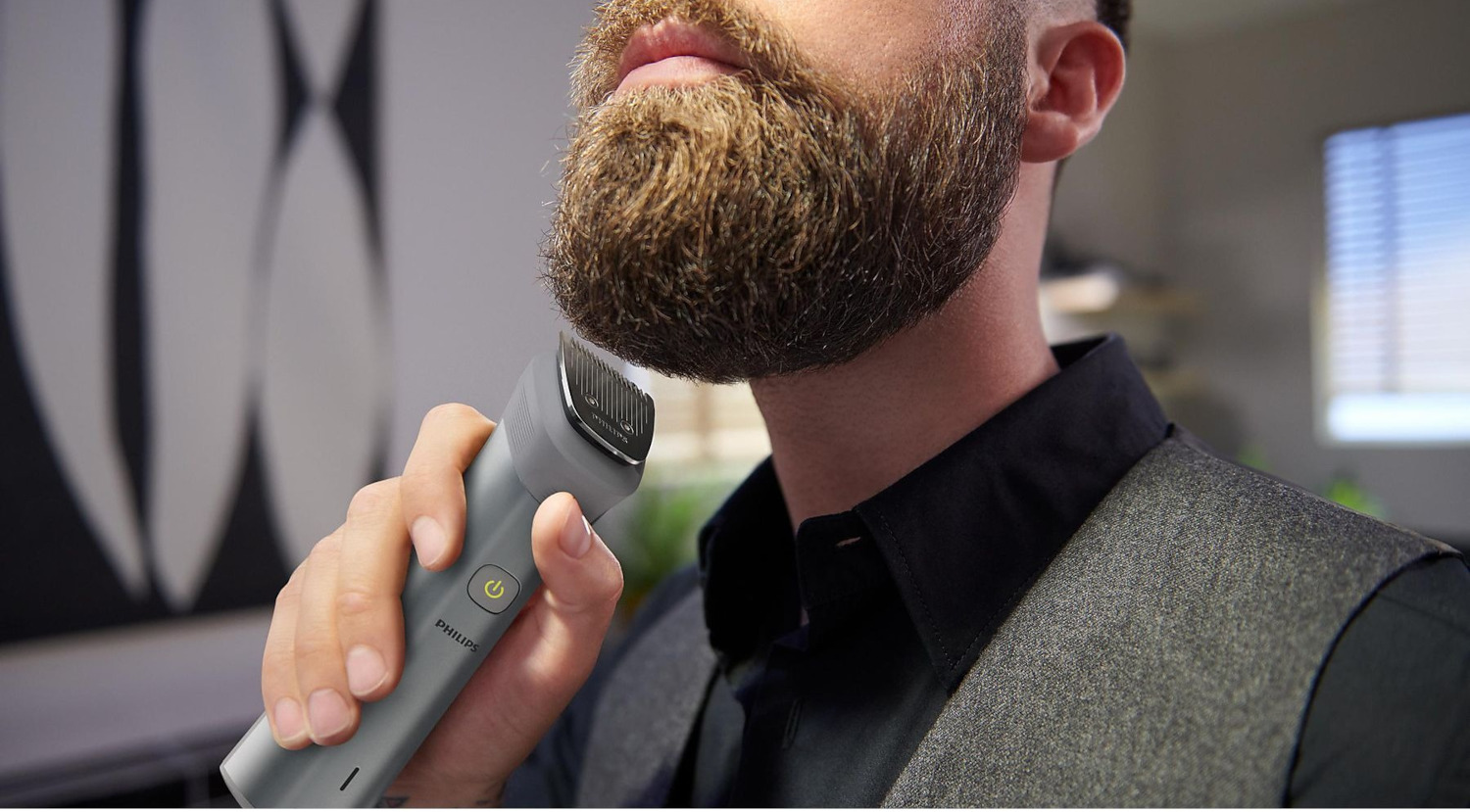 Homme taillant sa barbe avec une tondeuse, gros plan du visage et tondeuse, fond gris.