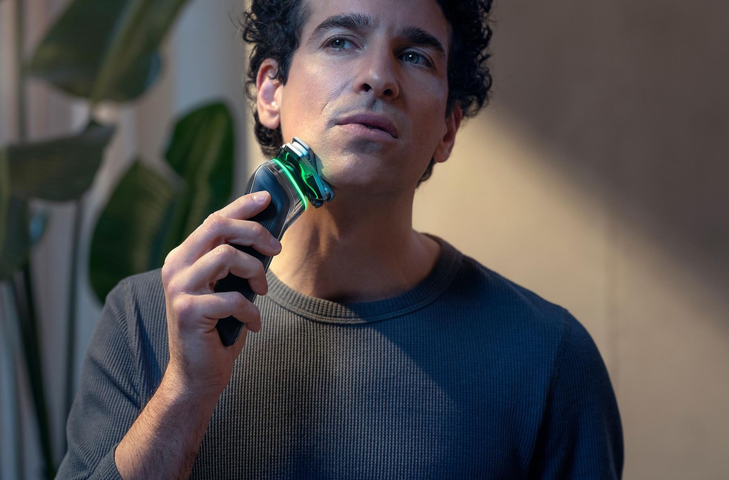 Un homme se rase avec un rasoir électrique, en gros plan, avec une lumière vive.