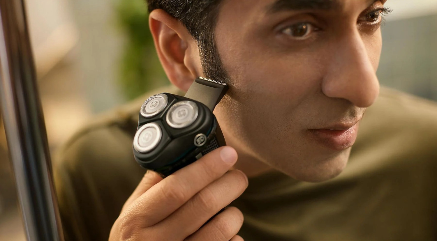 A man shaving his sideburns with an electric shaver, close-up shot.