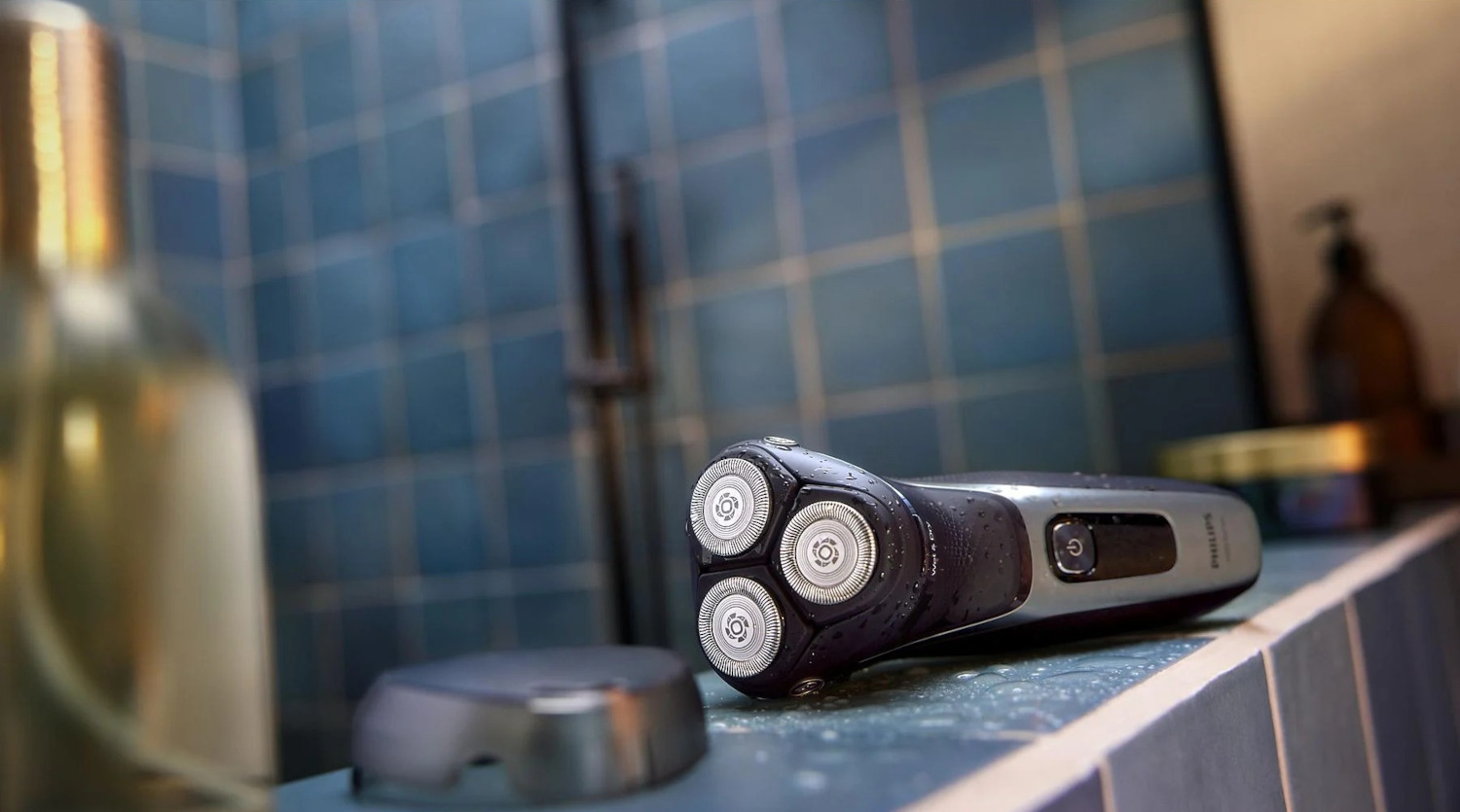 Electric shaver on a blue tiled surface. A bottle and a charging base are also in the scene.