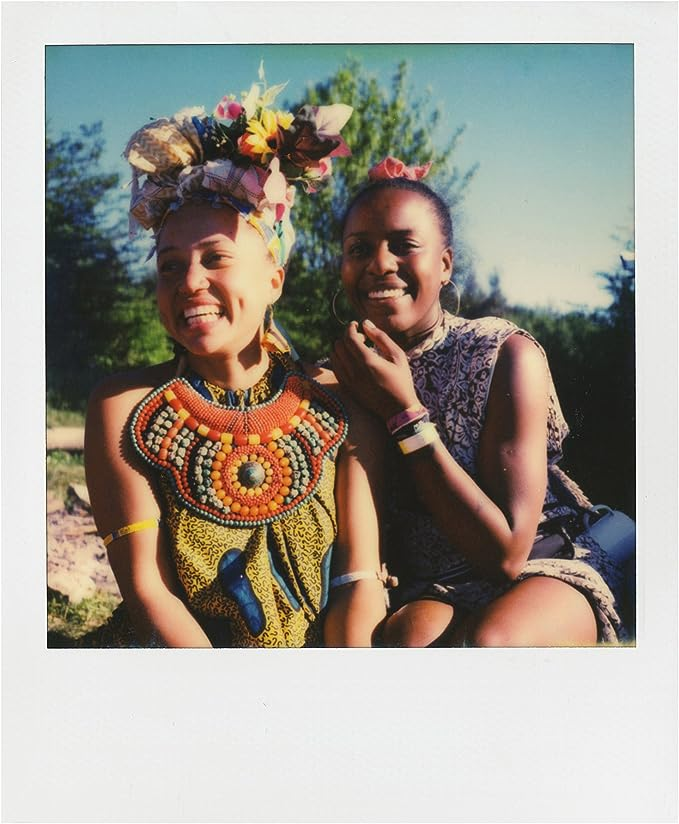 Dos mujeres sonriendo con atuendos coloridos, pañuelos y joyas.