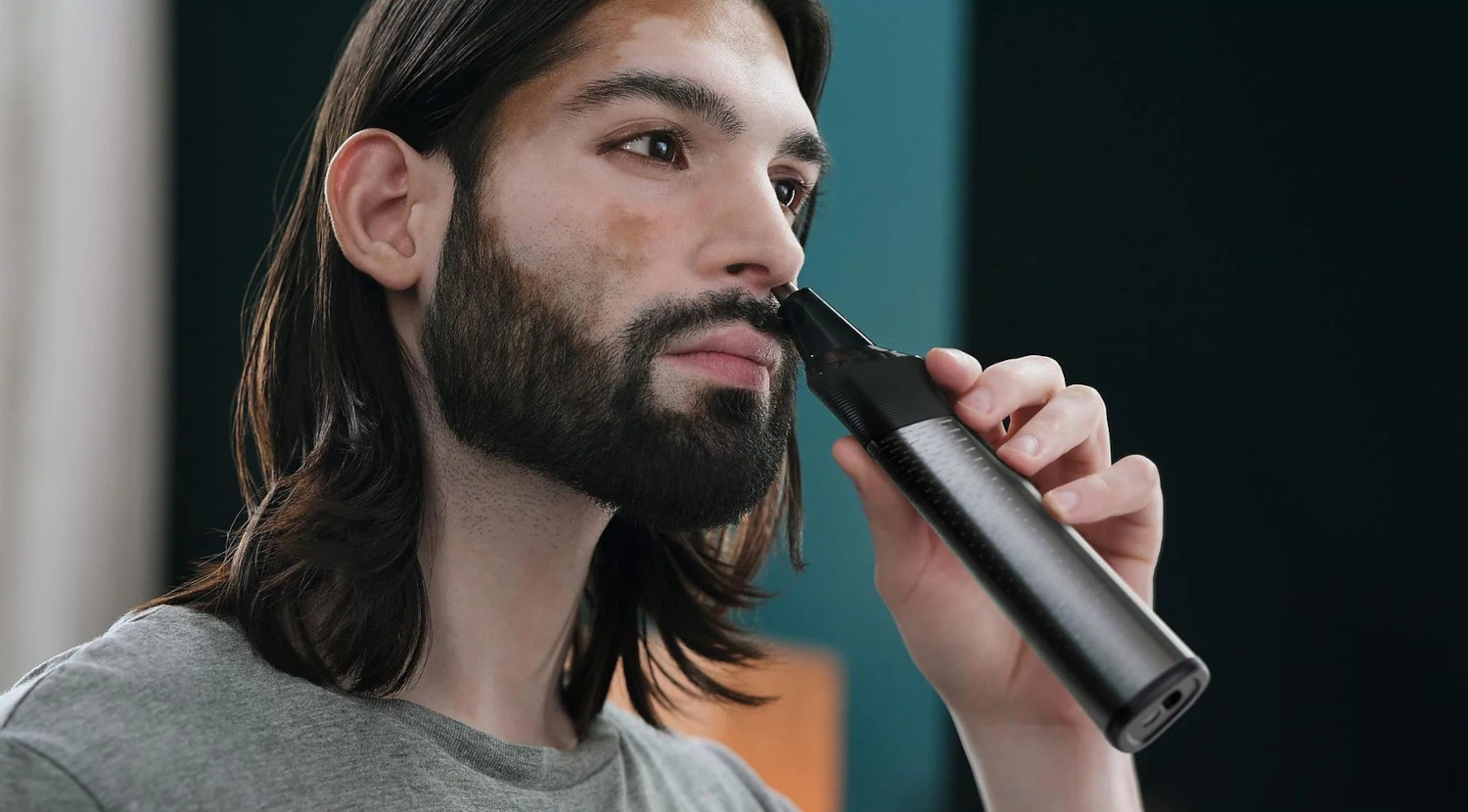 Homme aux cheveux longs utilisant une tondeuse à poils de nez.