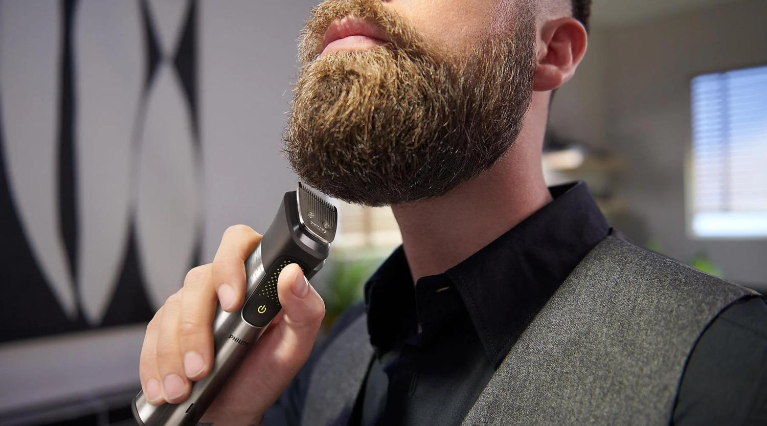 Homme taillant sa barbe avec une tondeuse noire et argentée.