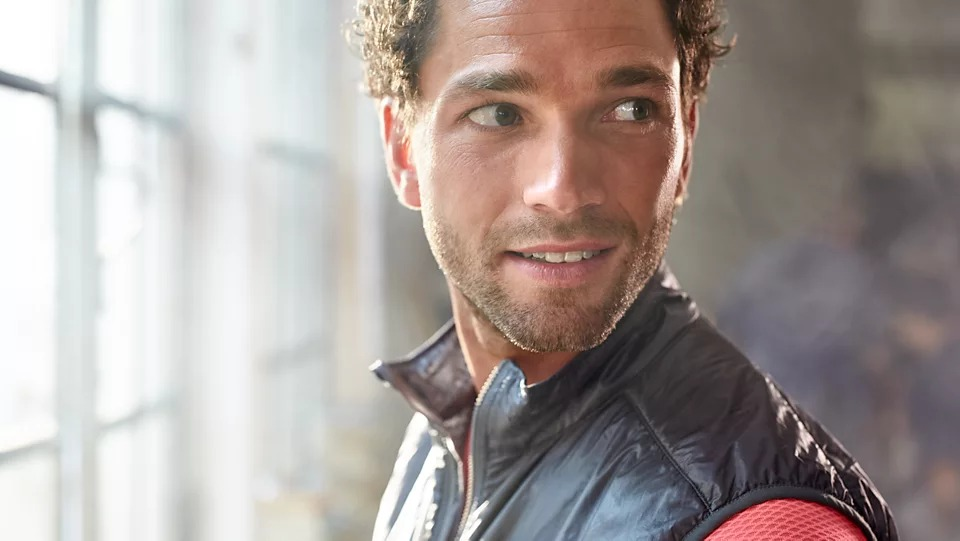 A man with a vest looks away, in a natural light setting.