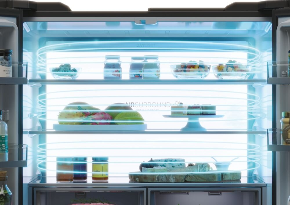 Otwarta lodówka z półkami z jedzeniem, oświetlona niebieskim światłem. Widoczne owoce, słoiki i ciasta.