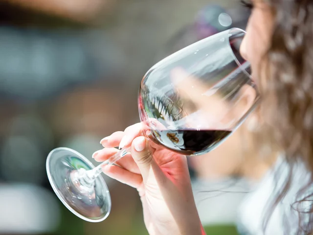 Donna che beve vino rosso da un bicchiere, primo piano, sfondo sfocato.