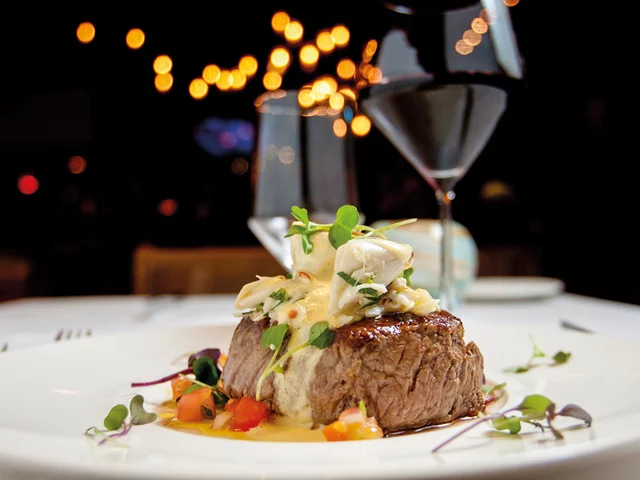 Una bistecca con carne di granchio in un piatto, vino rosso e sfondo sfocato.