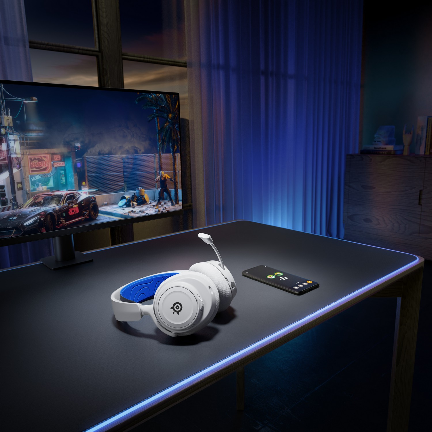 A gaming setup with headphones, phone, and monitor, black desk and blue lights.