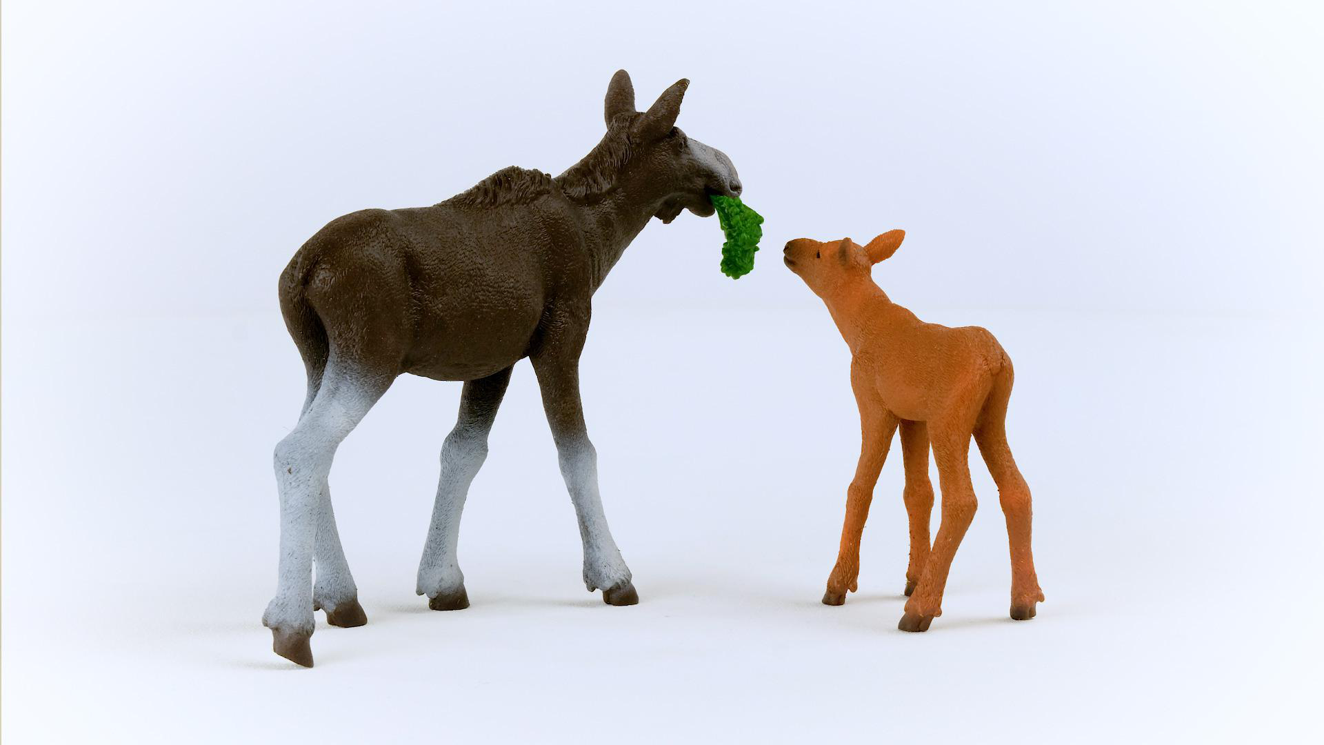 Zwei Spielzeugelche, einer füttert dem anderen grüne Blätter.