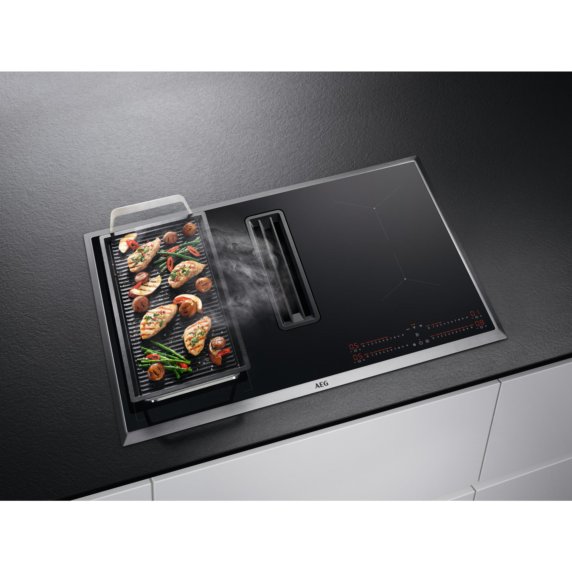 Ein AEG Induktionskochfeld mit integriertem Dunstabzug. Essen wird auf einer Grillplatte gegart. Schwarze Arbeitsplatte.