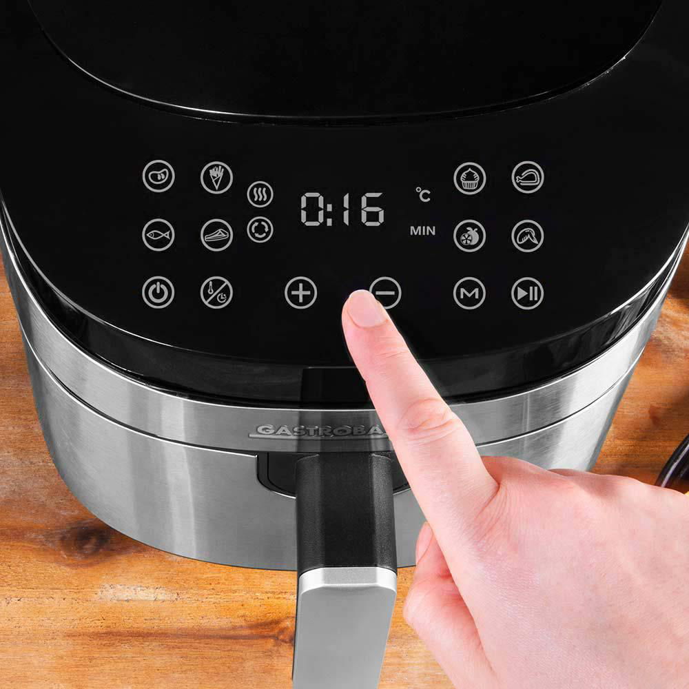 Eine Heißluftfritteuse mit Digitalanzeige, eine Hand drückt eine Taste. Die Anzeige zeigt Zeit und Einstellungen.