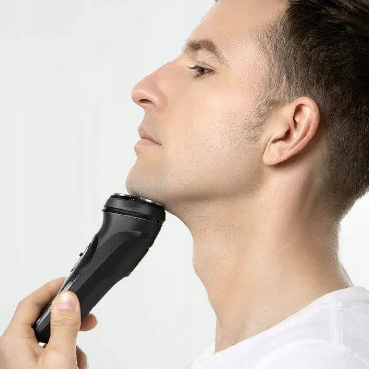 Mężczyzna goli twarz czarną golarką elektryczną.