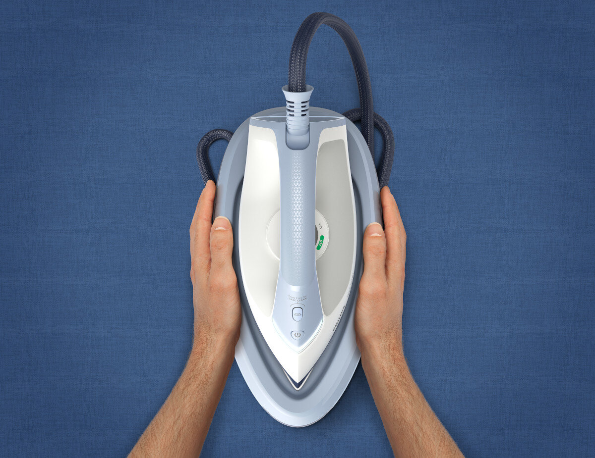 Dłonie trzymające niebiesko-białe żelazko nad niebieską powierzchnią, widok z góry.