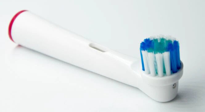 Biała końcówka szczoteczki do zębów z niebieskim i zielonym włosiem, czerwonym akcentem.