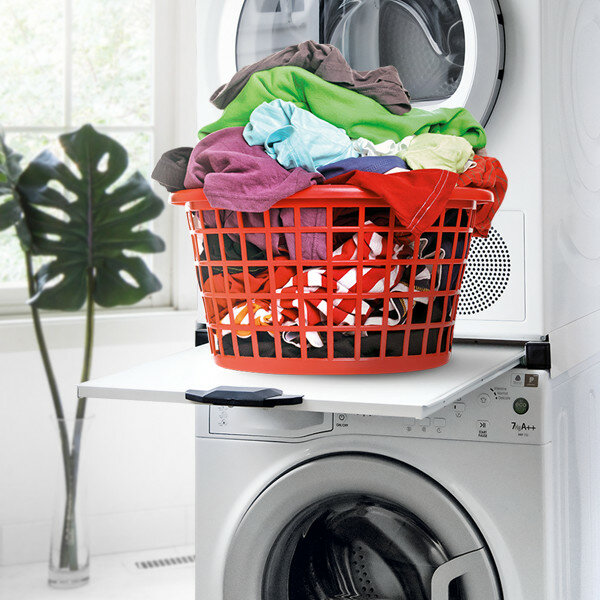 Czerwony kosz na pranie wypełniony ubraniami stoi na białej półce nad białą pralką.