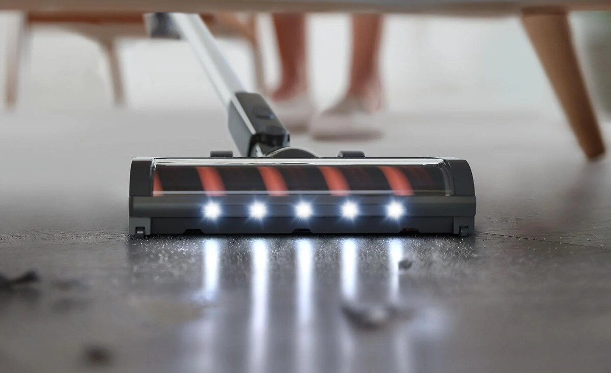 Głowica odkurzacza ze światłami, na podłodze z zanieczyszczeniami, stopy osoby.