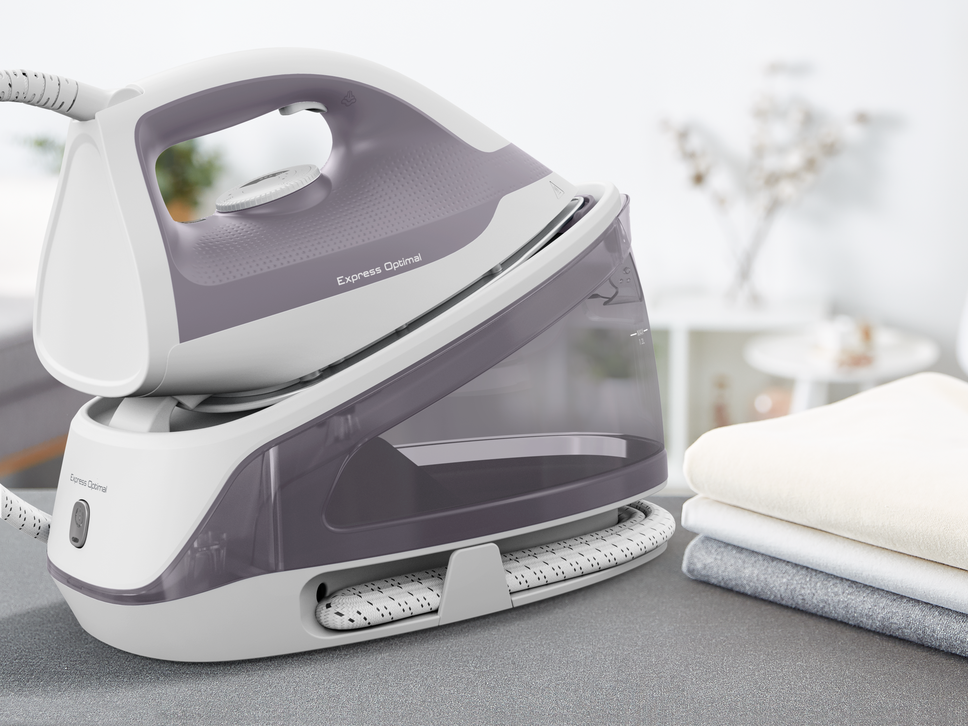 Tefal Express Optimal vasaló és talp. A vasaló lila és fehér, hajtogatott ruhák mellett az asztalon.