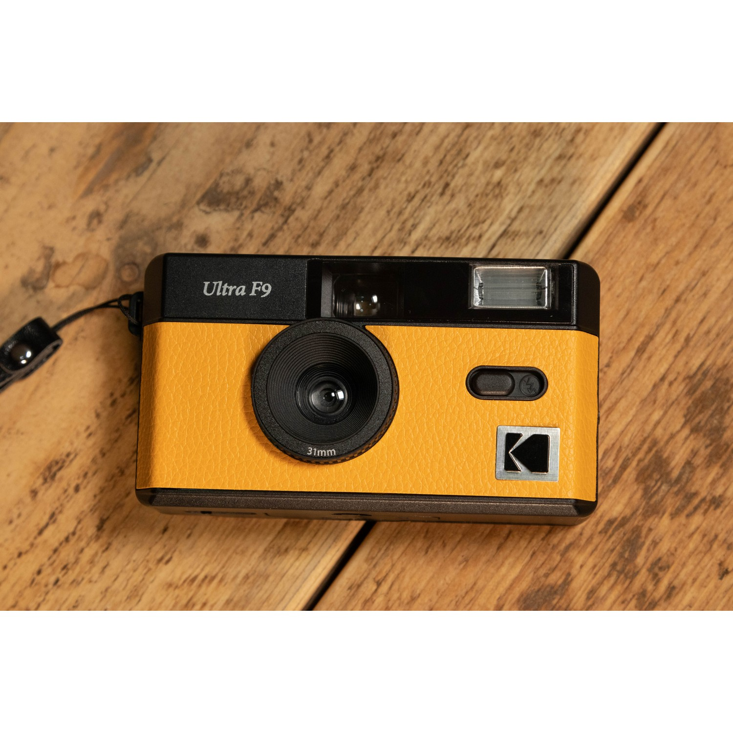 Yellow Kodak Ultra F9 camera on a wooden surface. It has a black lens and top, and a leather strap.