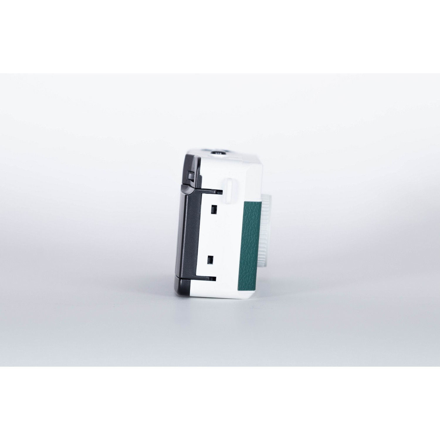 Small, white, and black camera. The camera has a green side. It is on a white surface.