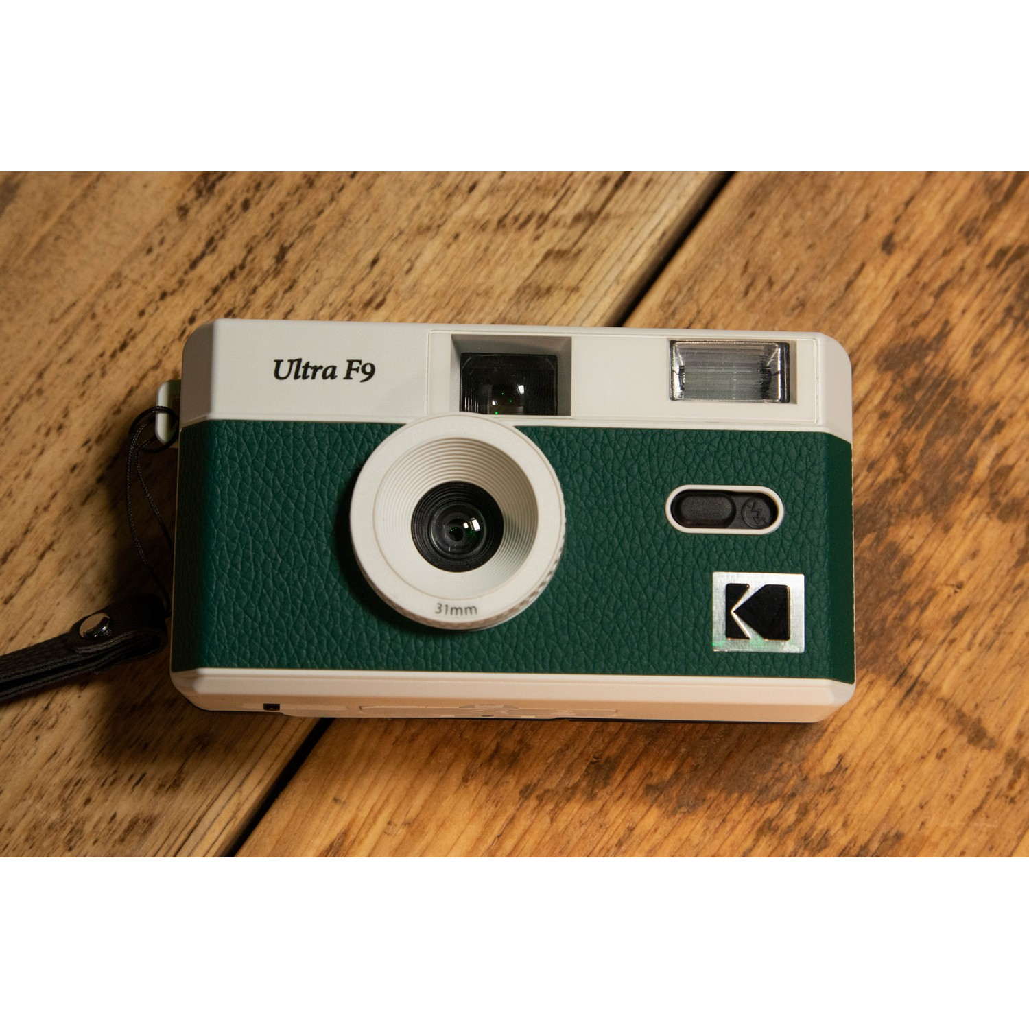 Retro camera in white and green, sitting on a wooden surface. The lens is centered.