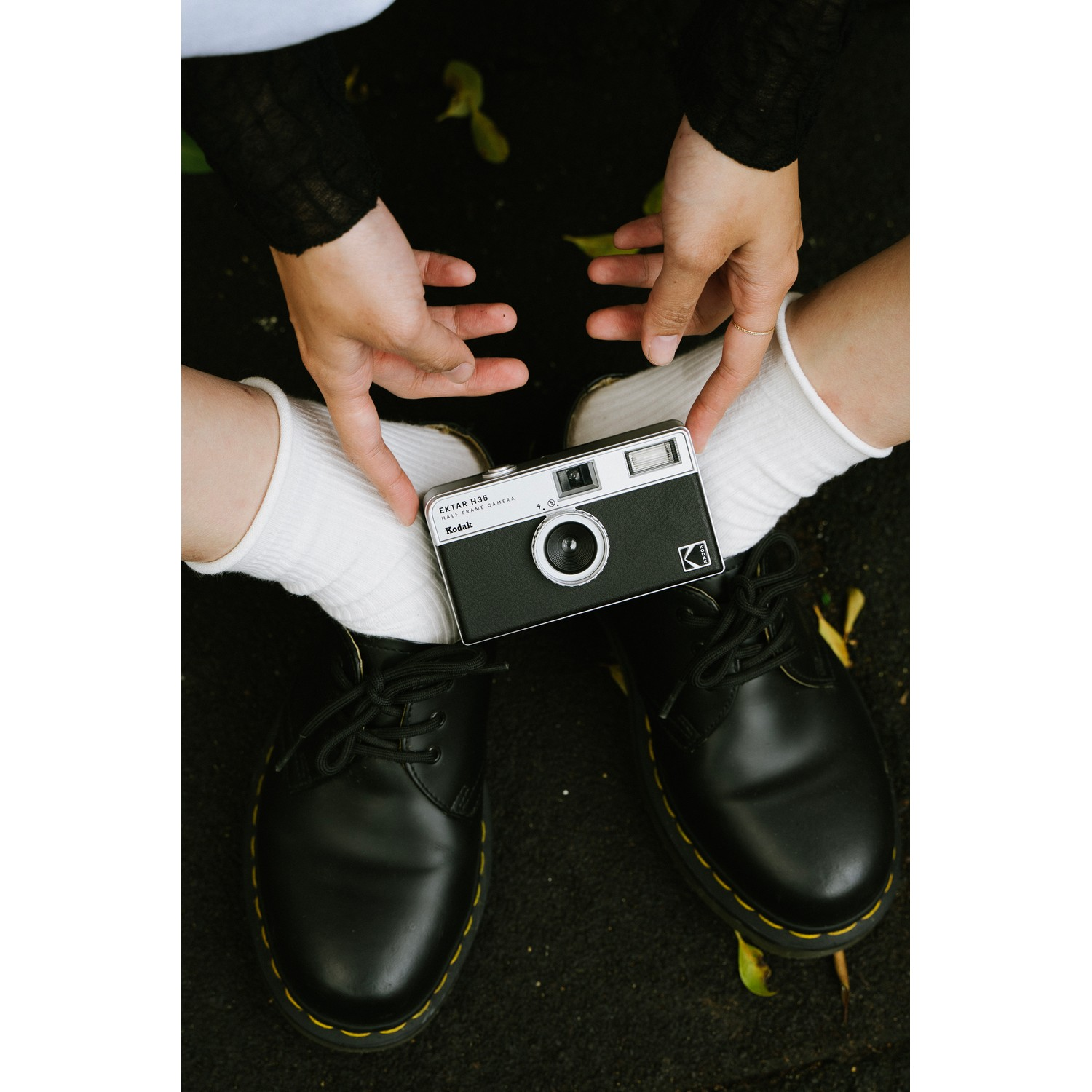 A person holding a black camera between their hands and legs.