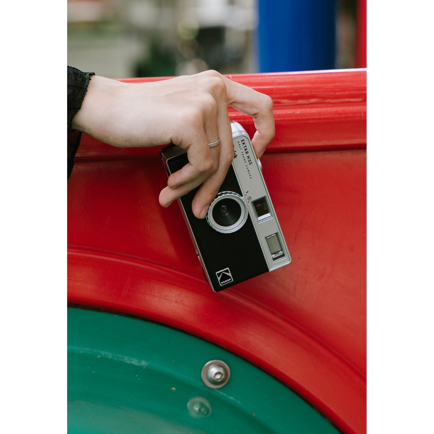 A hand holding a black and silver camera by a red structure.