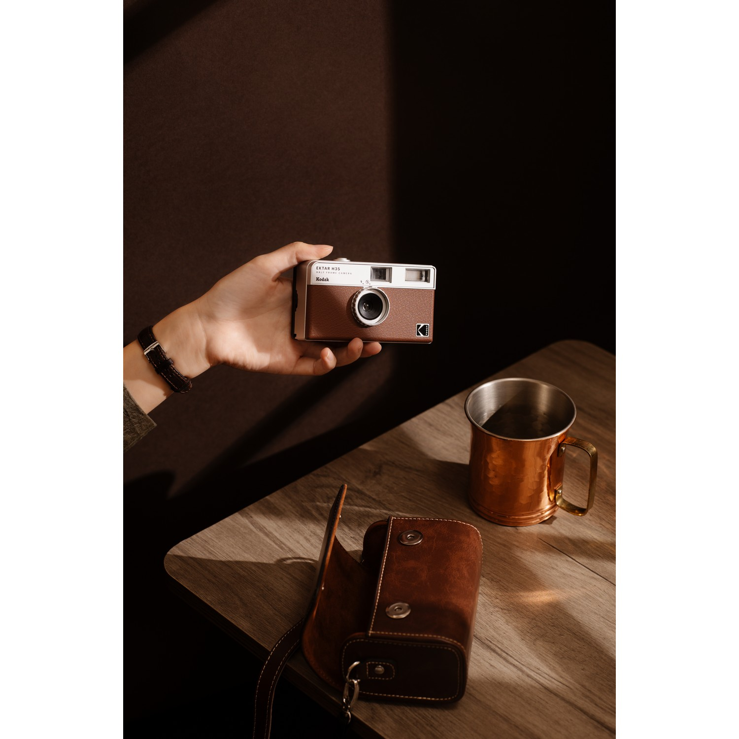 A person holding a brown camera and a copper mug, with a case.