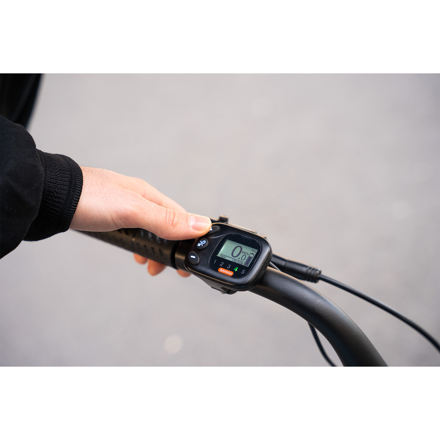La mano di una persona sul manubrio di una bicicletta mostra uno schermo elettronico. Lo schermo mostra velocità e impostazioni.