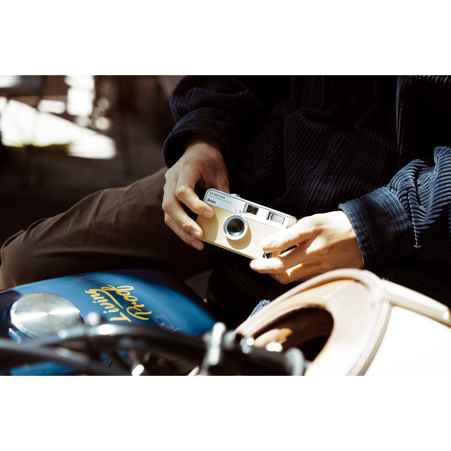A person holding a vintage camera, on a motorcycle seat.