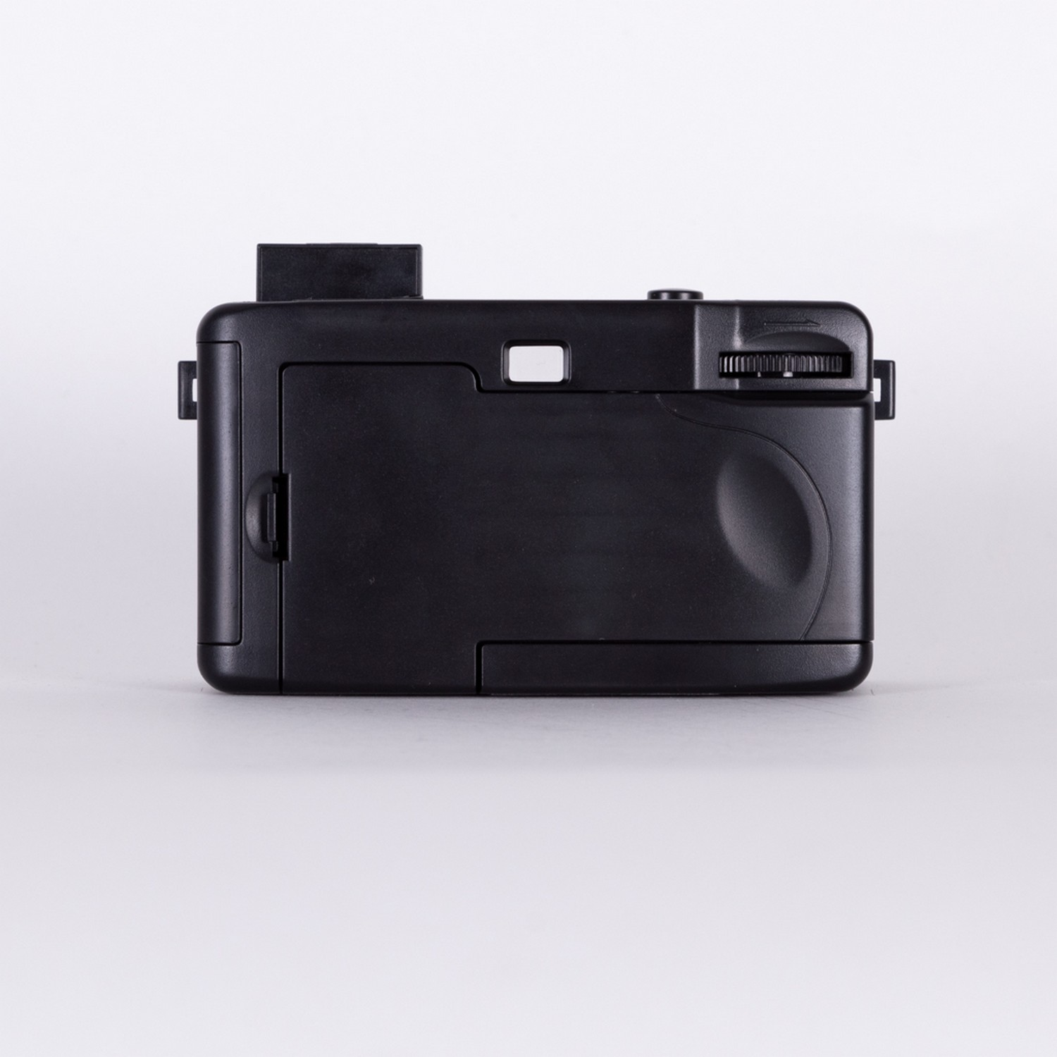 Black, rectangular camera. Rectangular viewfinder. Rounded dial for settings. Plain background.