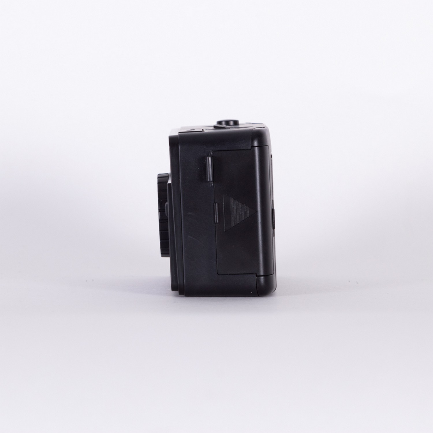 Black camera on a white surface. The camera is small and boxy, with a lens and buttons visible.