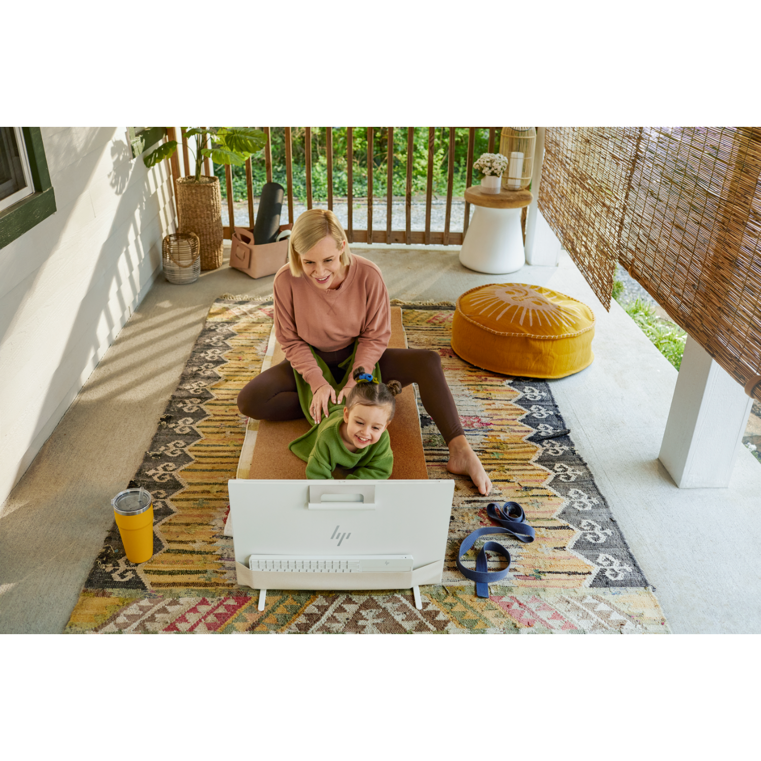 Vrouw en kind op een veranda die yoga doen, met een computer en yogamat.