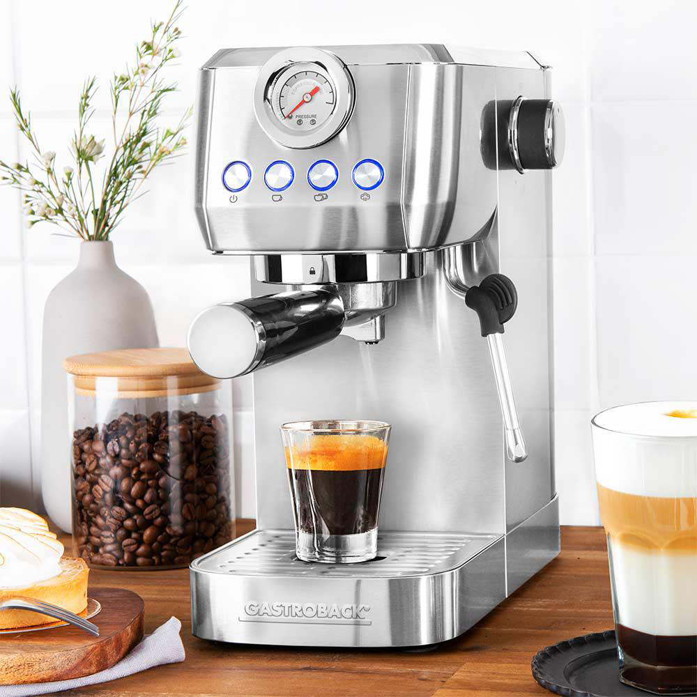 Eine silberne Espressomaschine mit einem Glas Espresso und einem Glas Latte auf einem Holztisch.