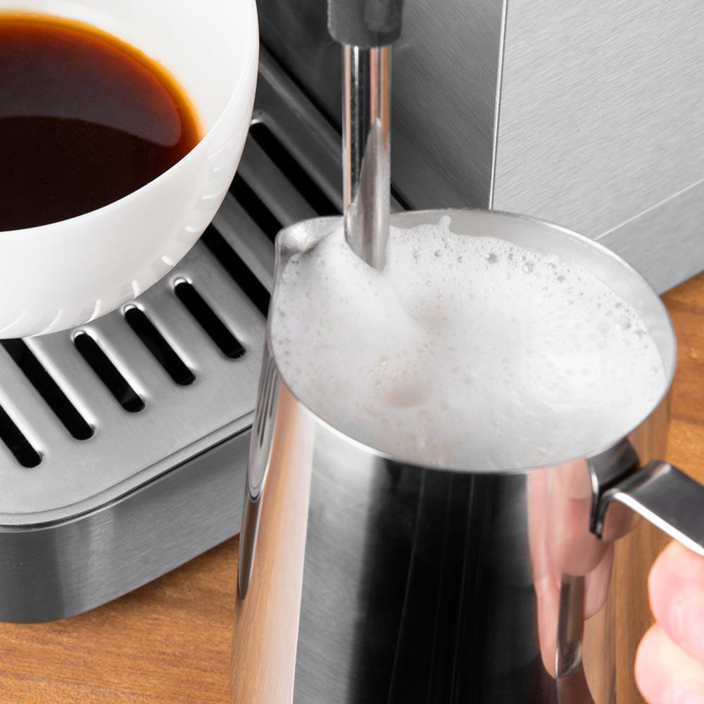 Espressomaschine, die Milch in einem Krug aufschäumt. Weiße Kaffeetasse daneben.