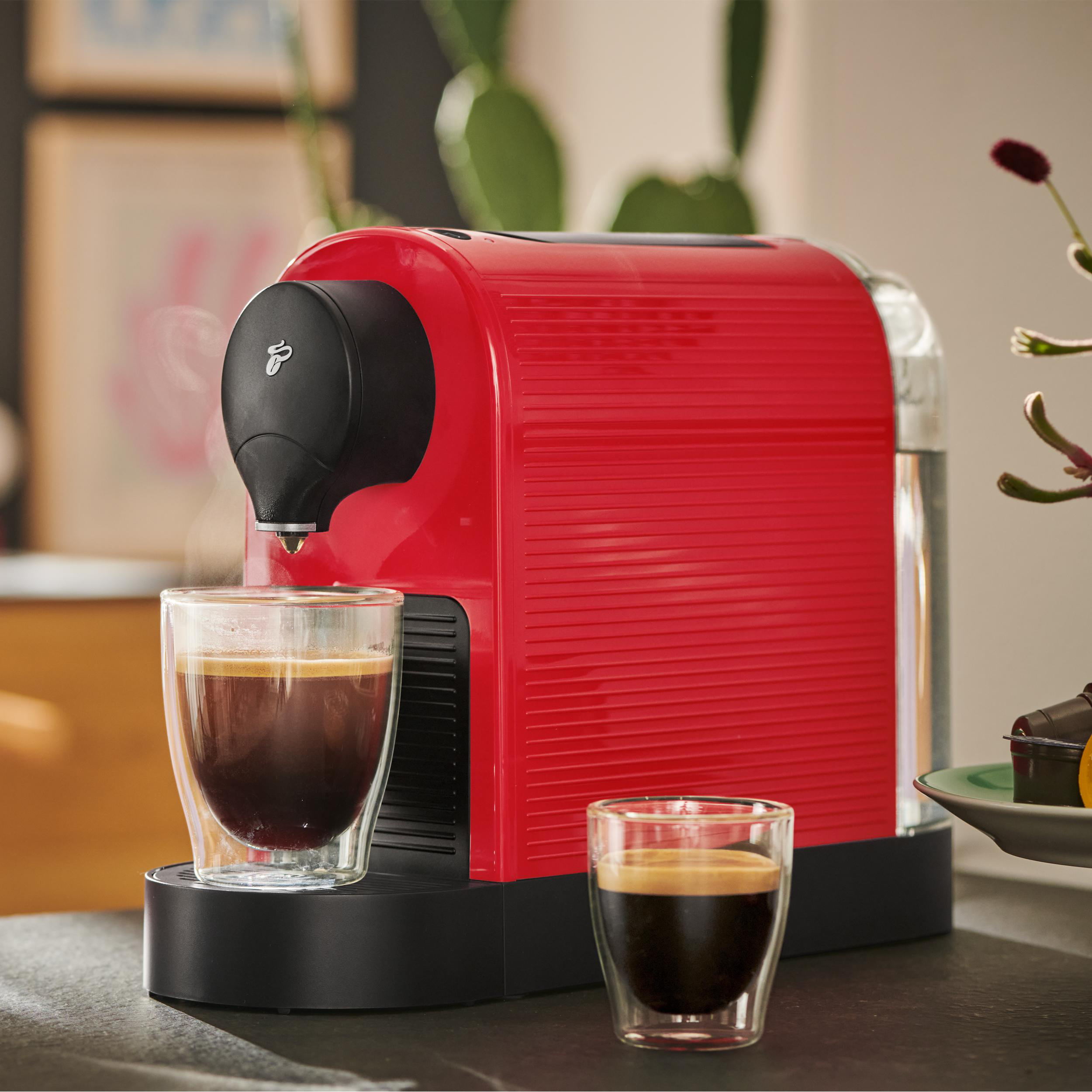 Rote Kaffeemaschine mit zwei Kaffeegläsern. Hintergrund ist eine Heimumgebung.