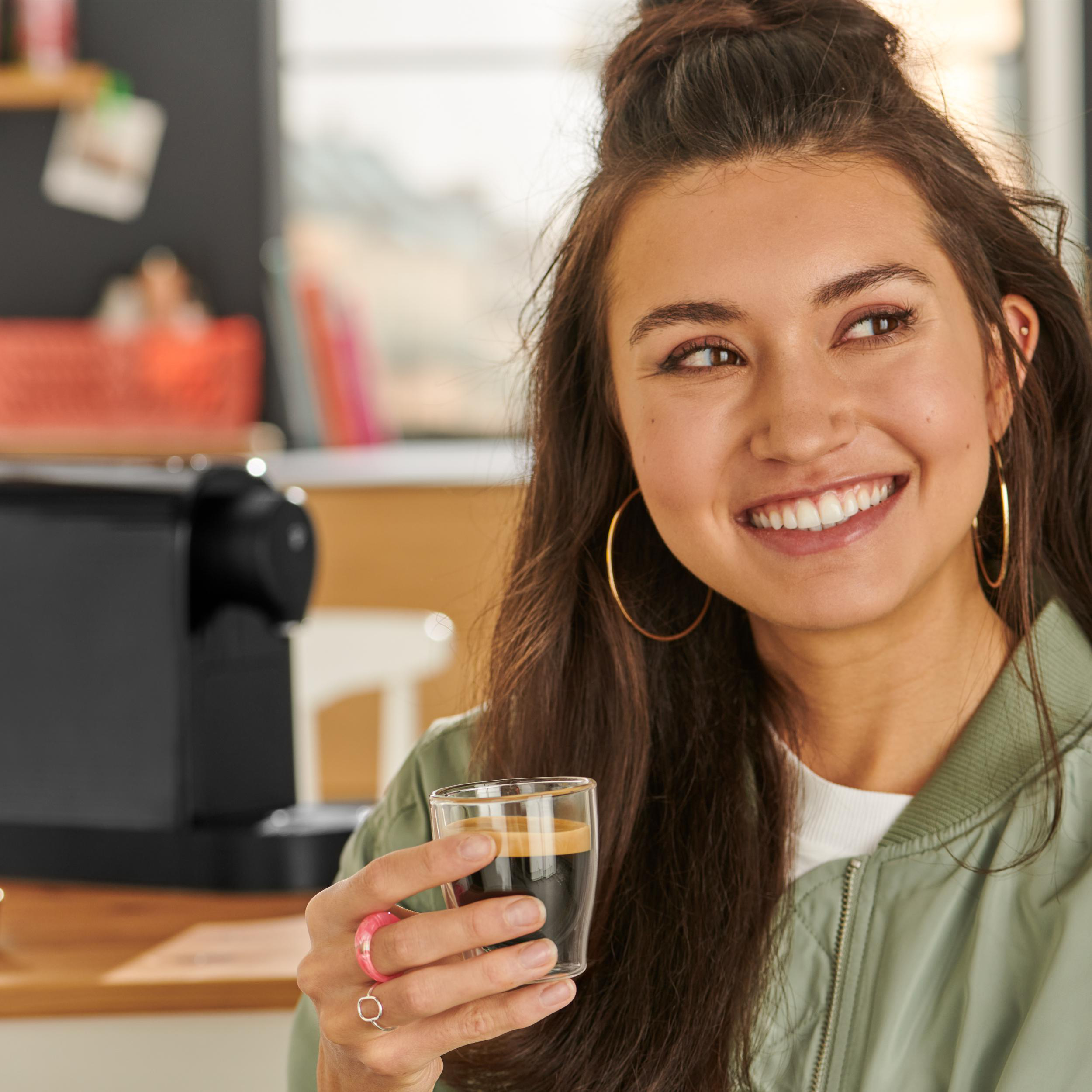 Lächelnde Frau, die ein Glas Kaffee hält und goldene Creolen trägt.