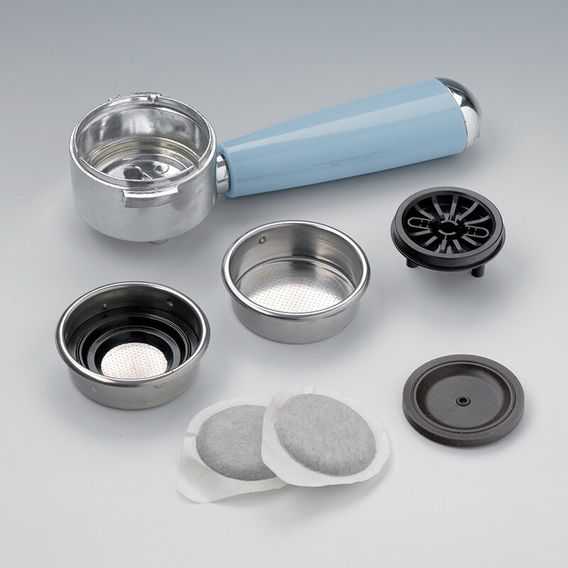 Części ekspresu do kawy: kolba, koszyki filtracyjne i kapsułki do kawy na jasnoszarej powierzchni.