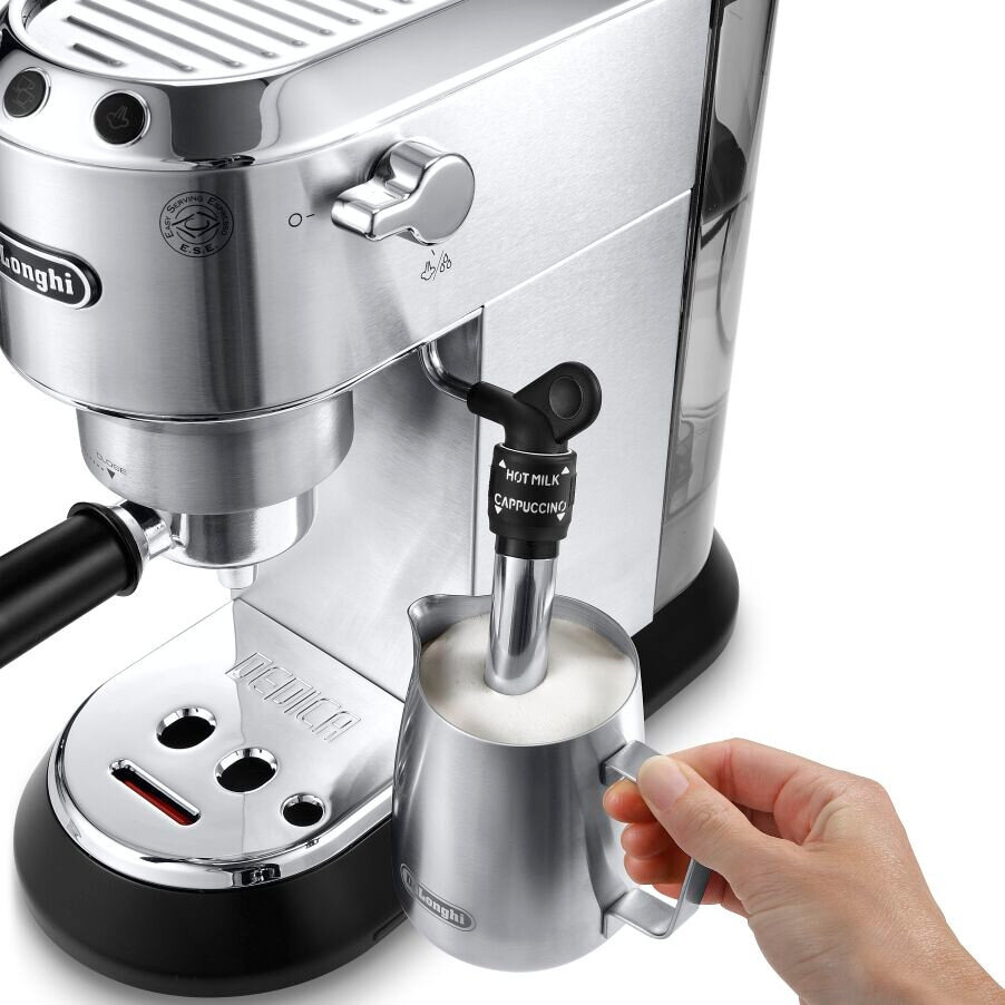 Ręka spienia mleko dyszą parową obok srebrnego ekspresu do kawy DeLonghi.