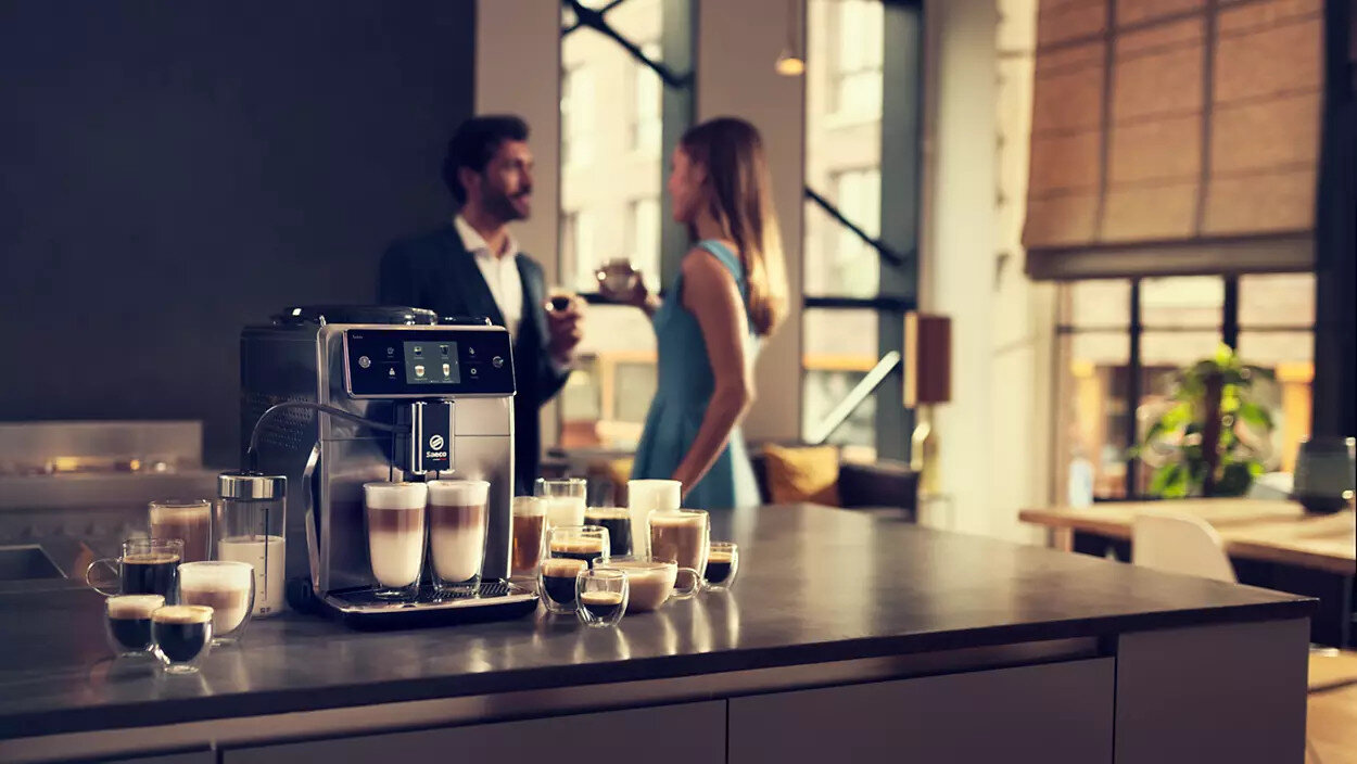 Ludzie w pobliżu ekspresu do kawy z różnymi napojami kawowymi na blacie kuchennym. Miękkie oświetlenie.