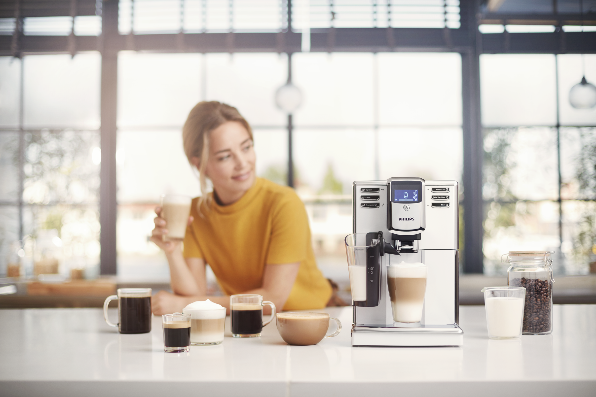 Kobieta z ekspresem do kawy, robi kawę z mlekiem i kilka filiżanek kawy.