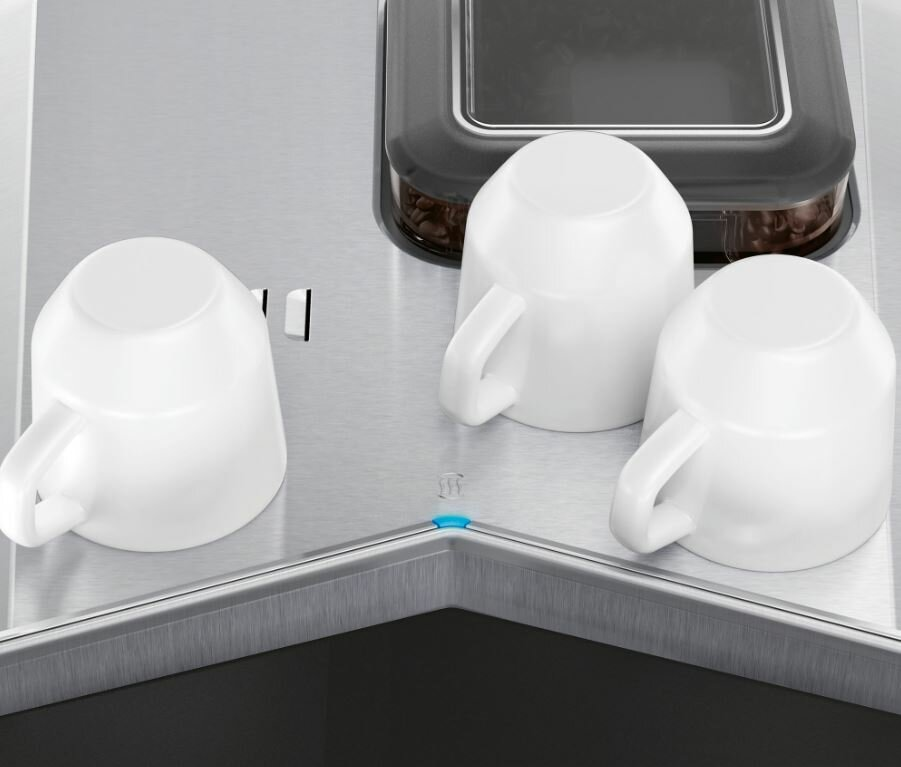 Trzy białe filiżanki do kawy stoją na ekspresie do kawy. Tło to stal nierdzewna.