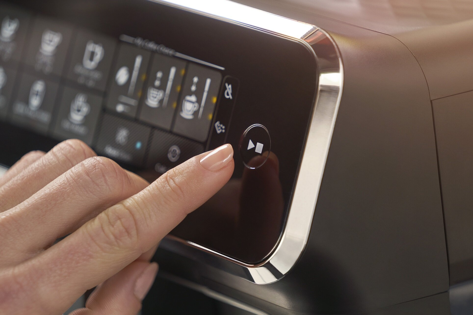 Zbliżenie dłoni dotykającej przycisku odtwarzania na panelu sterowania ekspresu do kawy.