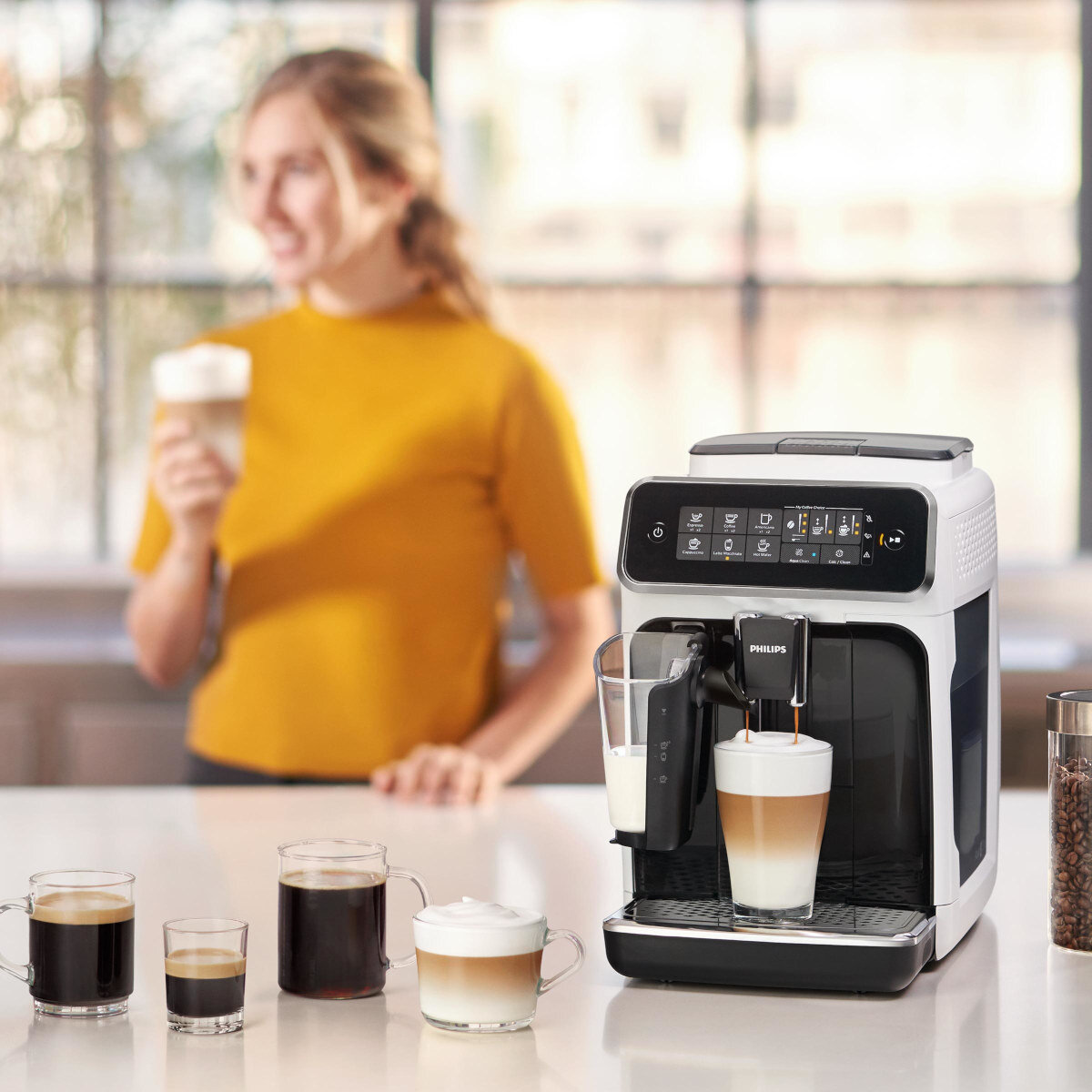 Ekspres do kawy robi kawę, z kobietą w tle trzymającą napój.
